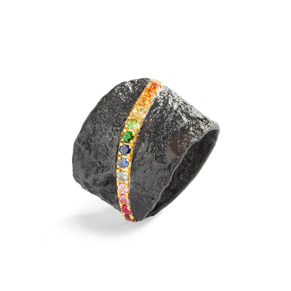 The November's Moon ring boasts a captivating blend of textures and colors, featuring textured blackened sterling silver contrasted with a vibrant 18k yellow gold bar adorned with multicolor sapphires. This sleek yet organic design creates a striking contrast between darkness and vivid hues, resulting in an artistic and visually arresting aesthetic.