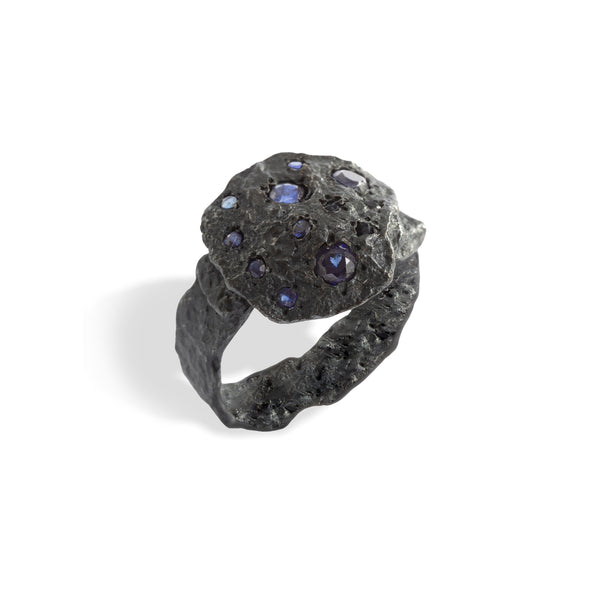 The November's Moon ring, crafted from blackened sterling silver adorned with blue sapphires, exudes a lunar charm. The contrast between the dark metal and the vibrant stones evokes a sense of the vast cosmos, merging the distant with the present.