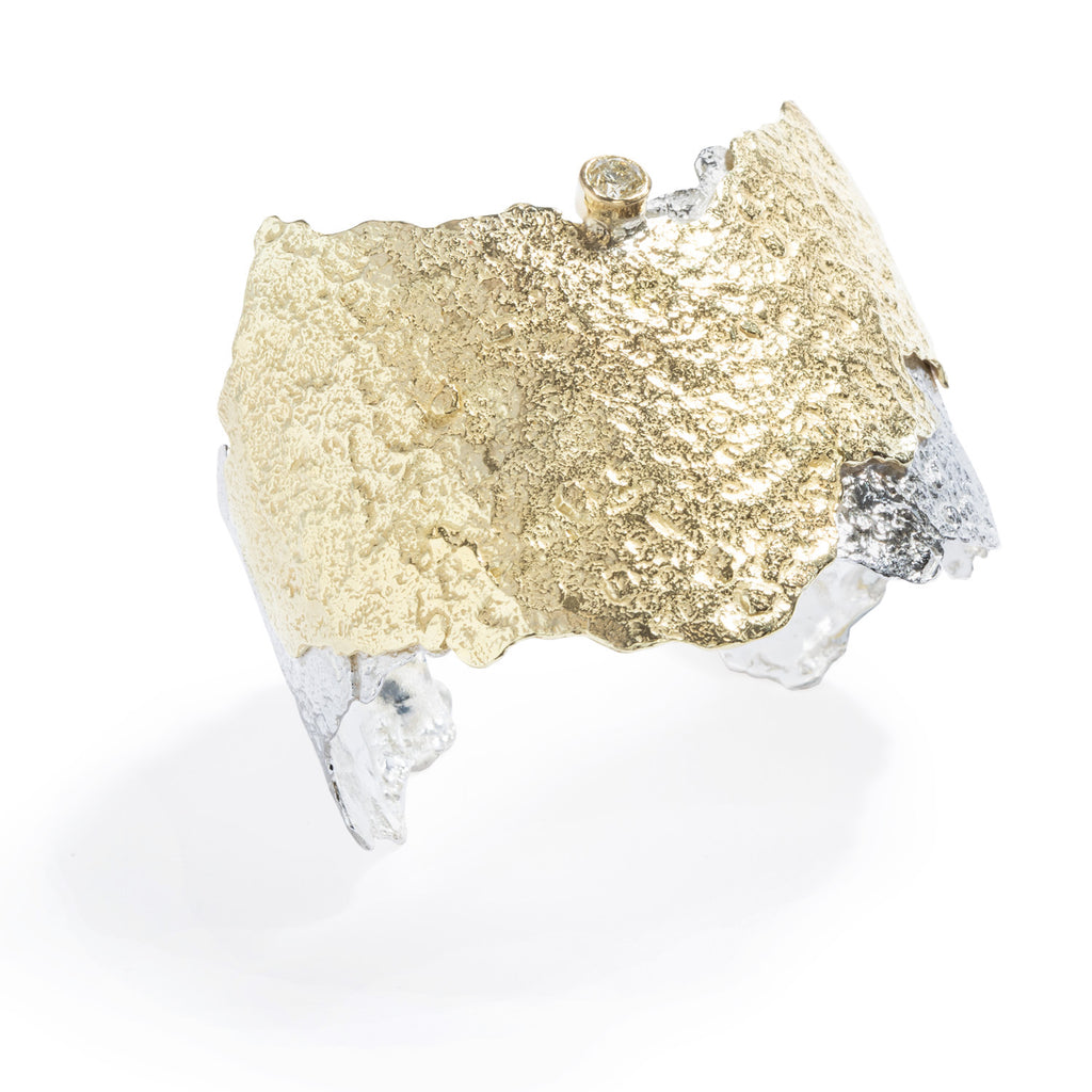 Good Vibes Gold & Silver Cuff with Diamond by Emanuela Duca - Crafted with a large textured 18K yellow gold edgy layer overlapping a layer of textured sterling silver, it epitomizes sophistication. Adorned with a breathtaking 5mm white/green diamond, it exudes unparalleled elegance and individuality. Elevate yourself with unique style and personality. One of a kind. Height: 2.25 inches.