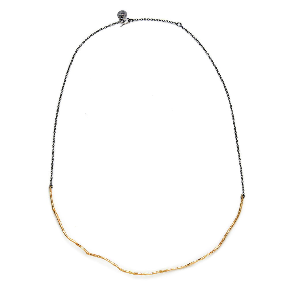 The Under a Tree necklace is a beautiful and refined piece that perfectly blends simplicity with character. This thin necklace features a solid, textured 18k yellow gold pendant, artfully suspended from a blackened sterling silver chain. The combination of rich, warm gold with the edgy, darkened silver creates a striking contrast that is both clean and elegant. 